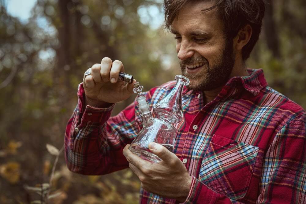 guy smoking out of a bong in the woods